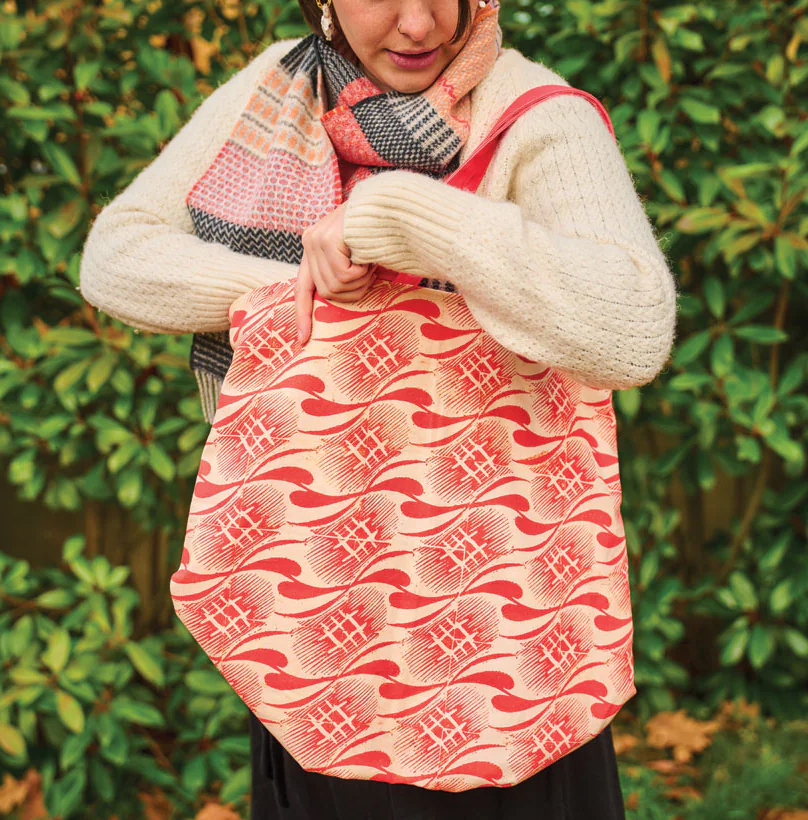 Photograph of a woman in white jumper with a red patterned tote bag on her shoulder