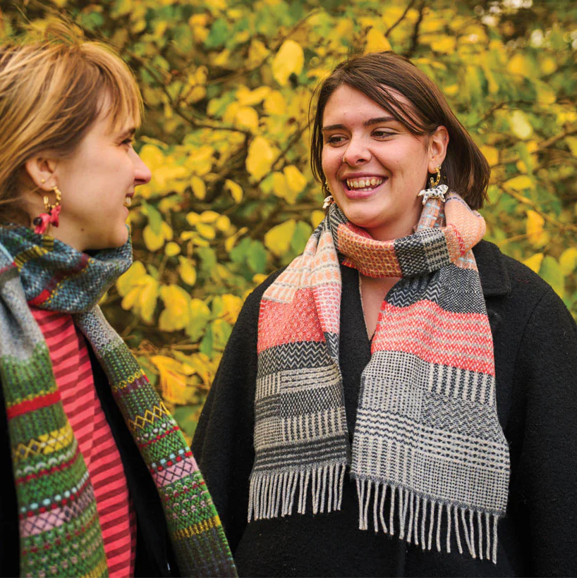 Photograph of two women wearing patterned scarfs looking at each other smiling